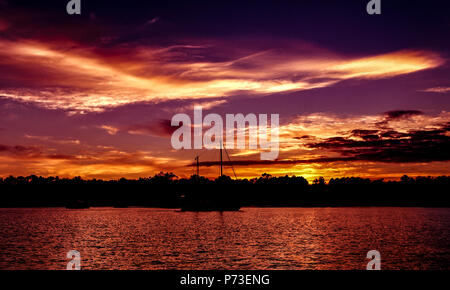 Einen spektakulären und bunten orange bewölkt tropischen Panoramablick Sonnenuntergang seascape mit Silhouetten mit Meerwasser reflecions. Australien. Stockfoto