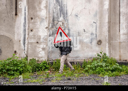 Unbekannter Mann hält eine rote Dreieck Warnschild vor seinen Kopf in der Nähe einer Ruine. Stockfoto
