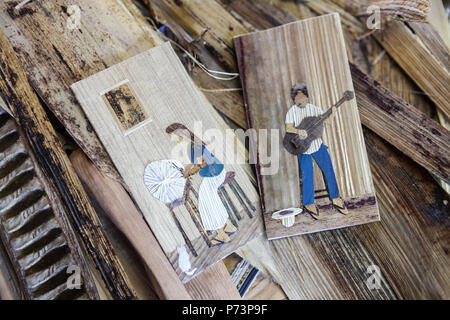 Florianópolis, Santa Catarina, Brasilien. Nahaufnahme von Bilder mit Mann spielt Gitarre und Frau Sticken mit Stroh und Holz. Stockfoto