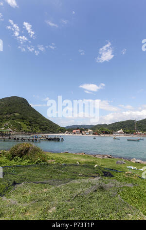 Florianopolis, Santa Catarina, Brasilien. Schöner Blick auf den Strand Landschaft mit fischernetze Trocknen auf das Gras und bunten Fischerbooten und Hügel wi Stockfoto