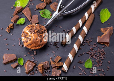 Schokoladeneis in Schaufel mit wafer Sticks und Schokolade auf schwarzem Schiefer. Fokus auf Eis in Schaufel. Stockfoto