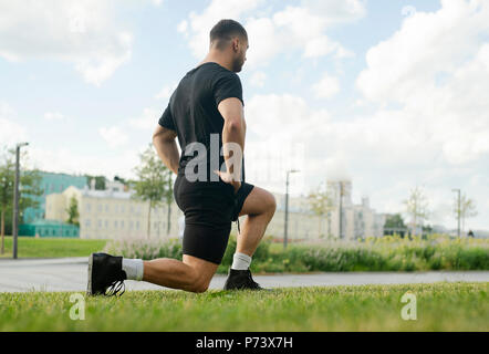 Jungen attraktiven Mann tun Ausfallschritt Outdoor im Park. Stockfoto