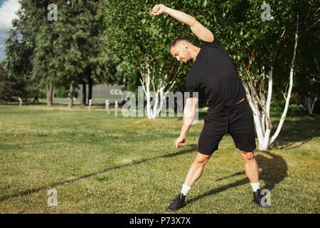 Attraktiver Mann zu tun Stretching Übungen mit Händen in Park. Stockfoto