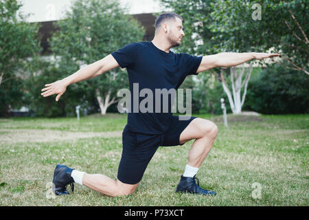 Jungen attraktiven Mann tun Ausfallschritt Outdoor im Park mit ausgestreckten Händen. Stockfoto