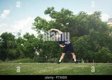 Attraktiven jungen Mann zu tun Stretching Übungen mit Händen Outdoor im Park. Stockfoto