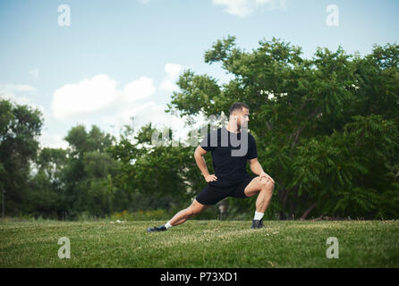 Jungen attraktiven Mann tun Ausfallschritt Outdoor im Park. Seitenansicht, fernen planen. Stockfoto