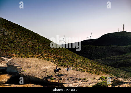 Paar Reiter mit Pferden in Abenteuer Freizeit Aktivität im Tal mit Bergen und Wind mühlen für die Energieerzeugung auf Hintergrund. Stockfoto