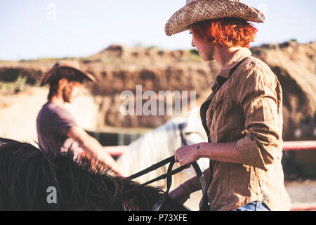 Paar der Moderne cowboy Ride zusammen. ein Mann und eine Frau mit zwei Pferde. warm filter Bild für alternativen Lebensstil und arbeiten oder Aktivitäten im Freien Stockfoto