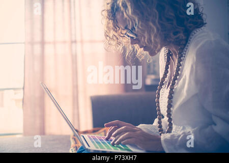 Schöne konzentrierte kaukasische Frau mittleren Alters Arbeiten am Laptop mit farbigen Suchbegriffe. Schriftsteller Arbeit zu Hause für alternativen Lebensstil und offic Stockfoto