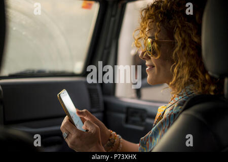 Eautiful Frau mittleren Alters check Handy für Ihr Profil auf Social Media während Reisen in ein Auto, wie Beifahrer. Technologie Smartphone mit Internetzugang Stockfoto