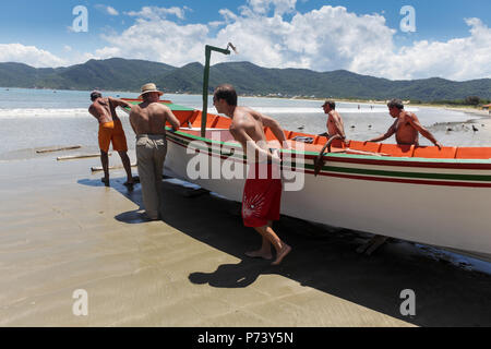 Florianopolis, Santa Catarina, Brasilien. Fischer treibt ein Boot ins Meer an einem sonnigen Tag am Strand. Stockfoto