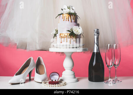 Paar Schuhe, Hochzeitstorte und Champagner isoliert auf Rosa Stockfoto