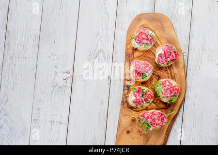 Leckere Vorspeise aus hauchdünn geschnittenem würzige Salami auf Brot mit Käse und Kräutern und Italienische Bruschetta mit Kräutern auf einem rustikalen Holzmöbeln Hintergrund Stockfoto