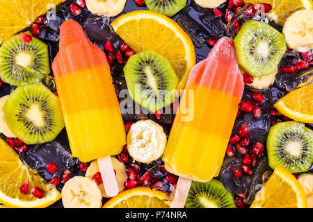Obst Eis auf Stick mit Scheiben Früchte auf schwarzem Schiefer. Fokus auf Eis am Stiel. Stockfoto
