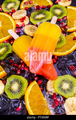 Obst Eis auf Stick mit Scheiben Früchte auf schwarzem Schiefer. Fokus auf Eis am Stiel. Stockfoto