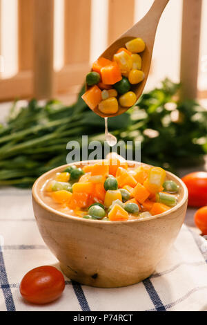 Schöpfkelle aus gedämpftem frisch geernteten jungen Gemüse, einschließlich Crinkle cut geschnittene Karotten, Erbsen und Kartoffeln für eine gesunde Begleitung zum Abendessen Stockfoto