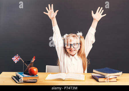 Junge Schüler Mädchen trägt smart Brillen steigen hands up lernen Englisch mit Buch vor dem dunklen Hintergrund Stockfoto
