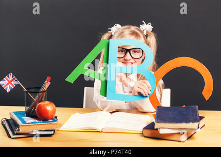 Junge Schüler Mädchen trägt smart Brillen halten bunte Buchstaben beim Lernen der Englischen Sprache mit Buch vor dem dunklen Hintergrund Stockfoto