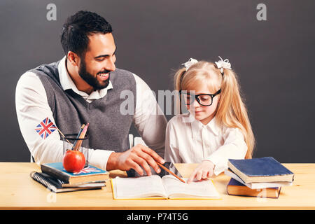 Intelligente männliche Lehrer erklären, neues Material auf der primären Schüler Mädchen am Tisch mit Büchern Stockfoto