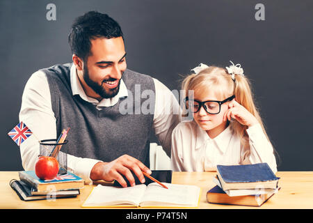 Intelligente männliche Lehrer erklären, neues Material auf der primären student Kind Mädchen am Tisch mit Büchern Stockfoto