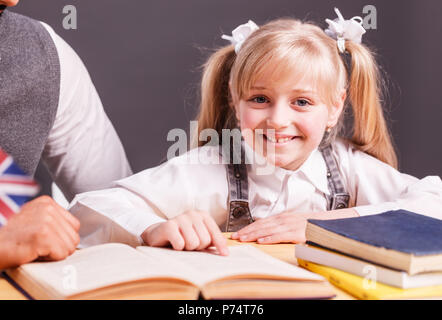 Erfolgreiche kid Schüler Mädchen lächeln beim Lesen Englisch Buch mit Lehrer helfen Stockfoto