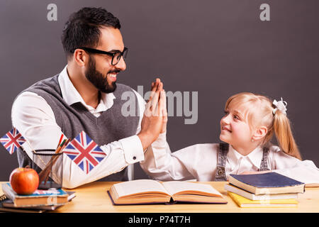 Erfolgreiche kid Schüler Mädchen lächeln, während die Hohe fünf beim Studium Englisch mit Lehrer Stockfoto