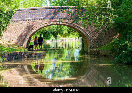 Zwei Wanderer und Ihren Hund zu Fuß den leinpfad unter einer Brücke neben dem Grand Union Canal in der Nähe von Crick, England im Sommer Stockfoto