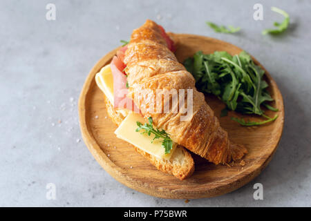 Leckere croissant Sandwich mit Schinken und Käse auf dem Holzbrett auf grauem Beton Hintergrund. Frühstück, Mittagessen oder einen Snack Sandwich Stockfoto