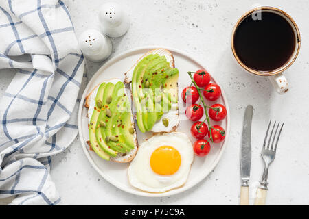 Avocado Toast, Eier und Kaffee zum Frühstück. Draufsicht auf das gesunde Frühstück. Zwei Toasts mit Avocado- und Frischkäse, sunny side up Ei, Cherry Tomaten Stockfoto