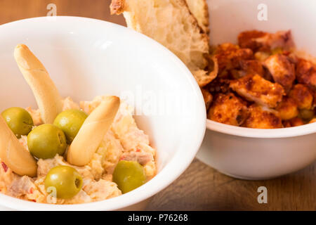 Russischer Salat in Keramik Schüssel mit Brot und Oliven. Ensaladilla rusa und Schüssel Octopus mit Kichererbsen und rote Paprika typisch für Galicien Stockfoto