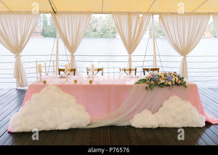 Die schöne Tabelle der Bräutigam und die Braut mit Blumen und Wolken eingerichtet. Eine Hochzeit in einem Zelt in der Nähe von Wasser Stockfoto