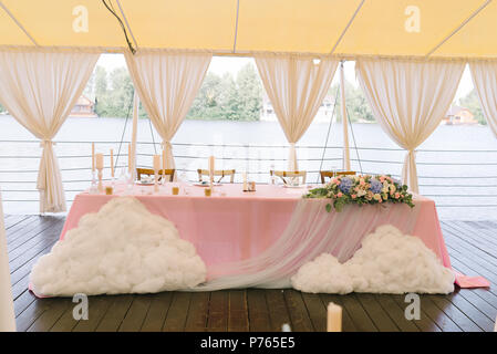 Die schöne Tabelle der Bräutigam und die Braut mit Blumen und Wolken eingerichtet. Eine Hochzeit in einem Zelt in der Nähe von Wasser Stockfoto