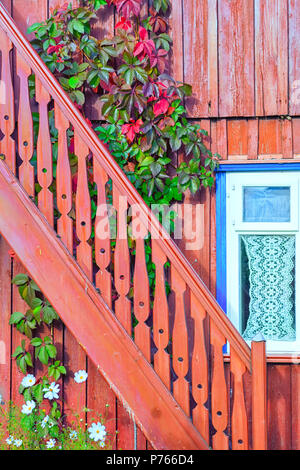 Eine anmutige aus Holz geschnitzte Treppe durch die Fenster mit einem Vorhang vor dem Hintergrund von Blumen und blühenden Efeu im Sommer Stockfoto