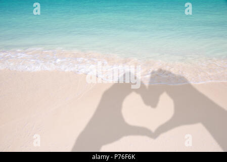 Schatten der Hände bilden ein Herz auf Sand und karibischen Strand Hintergrund Stockfoto