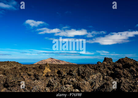 Die große Leere und Einsamkeit der Lanzarote schwarz gefrorener Lava vulkanische Wüste und einem Erodierten braune Hügel im Hintergrund Stockfoto