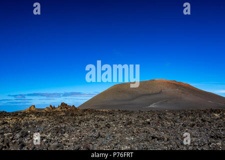 Die große Leere und Einsamkeit der Lanzarote schwarz gefrorener Lava vulkanische Wüste und einem Erodierten braune Hügel im Hintergrund Stockfoto