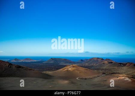 Wenn es nicht das Meer, das würde aussehen wie Moon scape. Die große Leere und Einsamkeit der Lanzarote schwarz gefrorener Lava vulkanische Wüste mit wenigen schlafende Vulkane und fast Clear blue sky Stockfoto