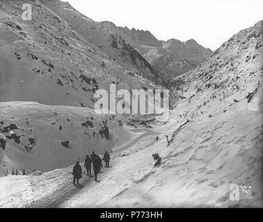 . Englisch: Klondykers wandern durch Cutoff Canyon, White Pass Trail, Alaska, Ca. 1898. Englisch: White Pass Hotel ist im Schnee in der Mitte des Bildes begraben. Auf der Rückseite des Bildes: "Cutoff Canyon auf der White Pass Trail. Beachten Sie die Zelte in der Mitte des Bildes alle aber mit Schnee bedeckt. Dies ist die Spur der Stampeder. Die White Pass und Yukon Railroad Kreise der Berg in der Mitte des Bildes, in der Mitte." Bildunterschrift auf das Bild: "Nach unten schauen. Cutoff Canyon anzeigen White Pass und Yukon RR auf dem Berg' Bild im Hegg Album 9, Seite 36. Original Foto von Eric A. Hegg Stockfoto