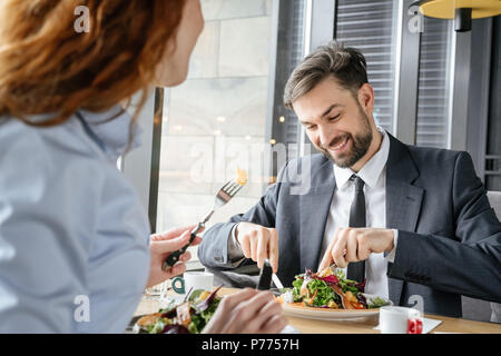 Mann und Frau in Business Lunch im Restaurant am Tisch Geschäftsmann sitzt das Essen von frischem Salat konzentriert lächelt glücklich halten Messer und Gabel bu Stockfoto