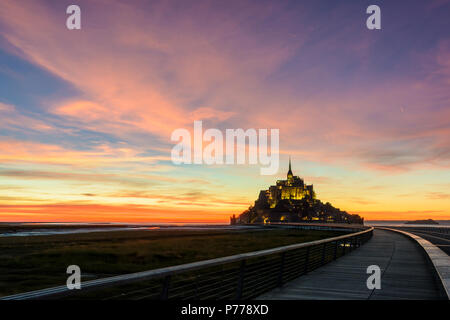 Blick auf den Mont Saint-Michel tidal Island in der Normandie, Frankreich, bei Einbruch der Dunkelheit mit dem hölzernen Steg im Vordergrund und lila Wolken im Himmel. Stockfoto