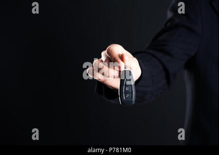 Autoverkäufer Übergabe ihres neuen Autoschlüssel, Händler und Vertriebskonzept auf einem dunklen Hintergrund Stockfoto