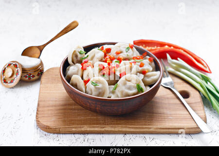 Gekochte Klöße in einem Ton Schüssel mit Pfeffer und Zwiebeln auf ein Holzbrett. Stockfoto