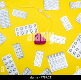 Rotes Herz und Katheter auf gelbem Hintergrund in der Mitte der Pakete mit weißen Tabletten, full frame Stockfoto