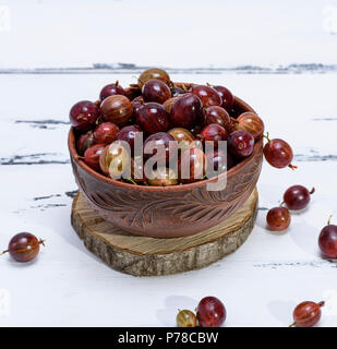 Reife rote Beeren von Stachelbeeren in einem braunen Ton Schüssel auf eine weiße Holztisch Stockfoto