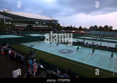 Das bodenpersonal die Abdeckungen auf der Außenseite Gerichte entfernen Nach einem zweiten Regen verzögert an Tag drei der Wimbledon Championships in der All England Lawn Tennis und Croquet Club, Wimbledon. Stockfoto