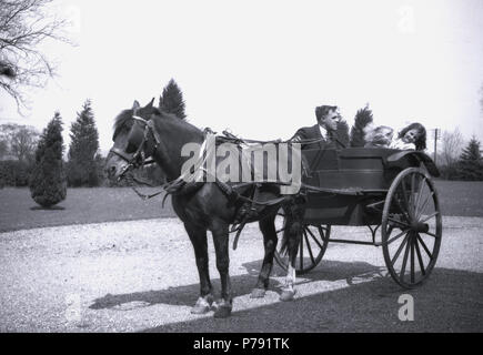 1930er Jahre, historische Bild, ein Mann (Treiber oder Kutscher?) sitzt mit zwei Mädchen in einer offenen Pferdekutsche Trap oder Buggy auf der Kies Zufahrt, England, UK. Stockfoto