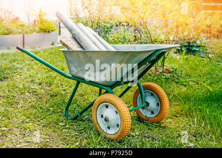 Nahaufnahme eines alten Schubkarre für den Transport von Gütern im Garten mit Rohren auf dem Hintergrund von einem grünen Garten. Stockfoto