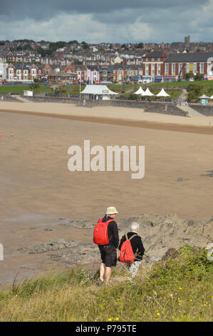 Zwei Menschen zu Fuß entlang der Küste weg über den Strand und die Bucht bei Barry Island bei Ebbe Stockfoto