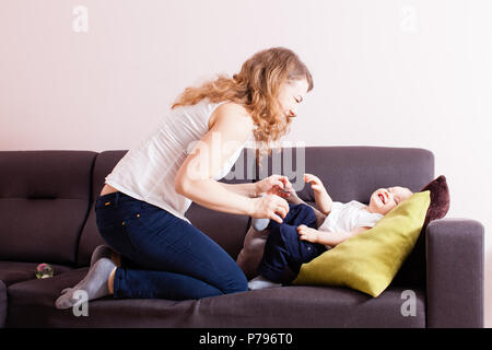 Junge Mutter loughing kitzeln Ihr adorable Toddlersohn auf Ihrer Couch. Stockfoto