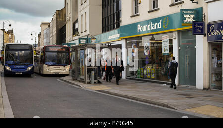 Zwei Busse in Cheltenham Town Centre mit einer Bushaltestelle und wartenden Fahrgäste im Vordergrund. Stockfoto